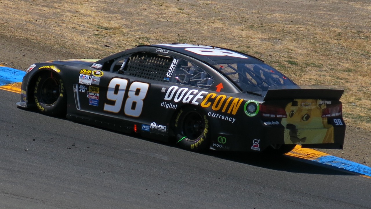 the real dogecoin #98 car at sonoma in 2014: black stock car, gold 98 on the door, dogecoin digital currency on the side, a doge on the rear deck